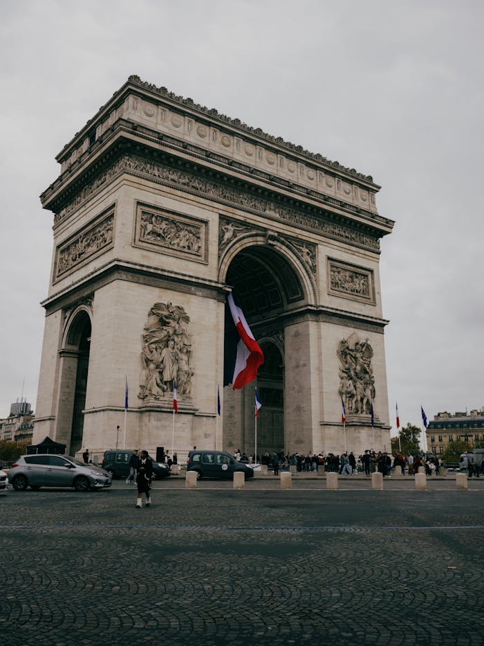 The iconic Arc de Triomphe with French flag on a cloudy day in Paris.