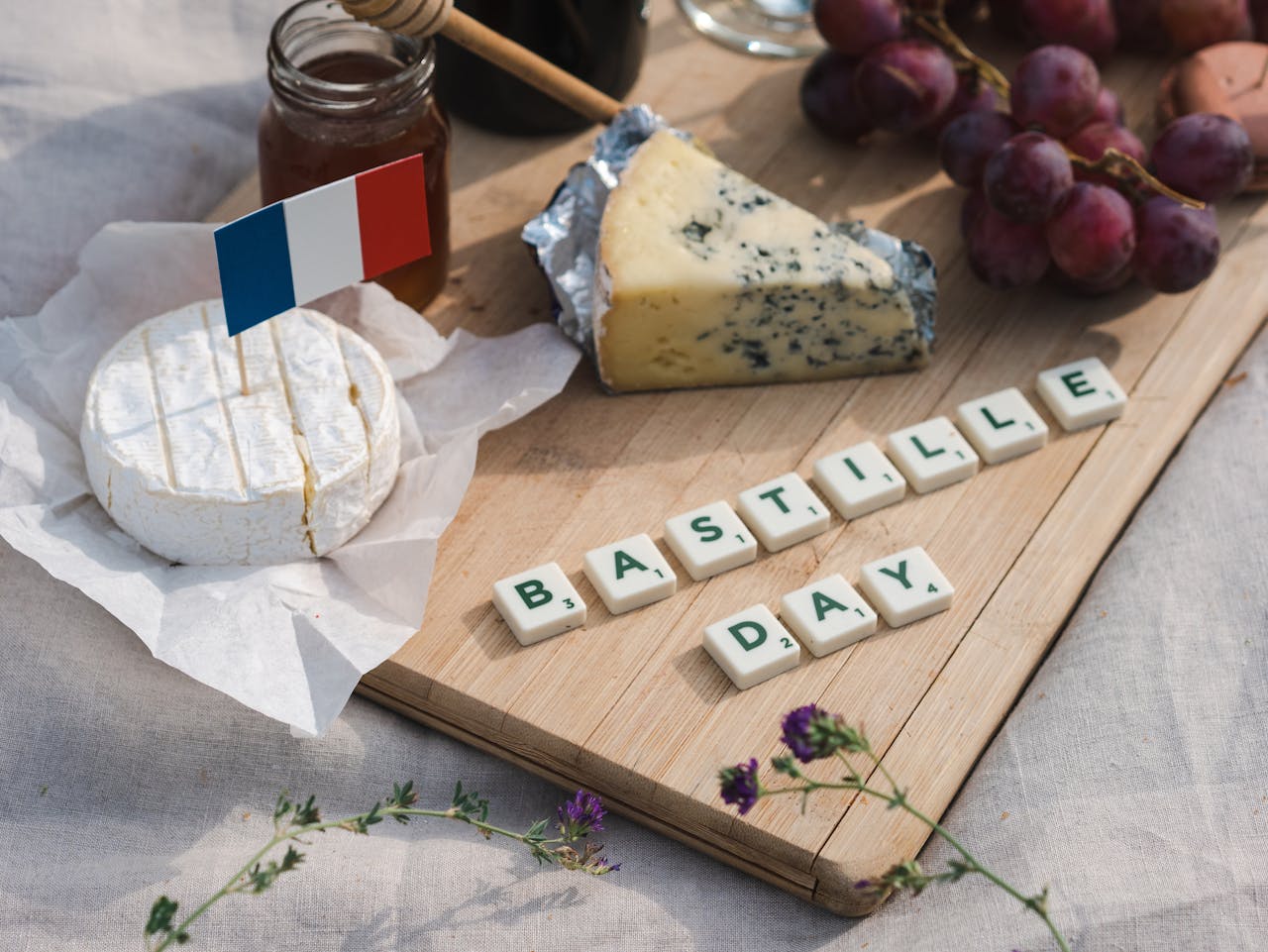 Celebrate Bastille Day with a festive picnic featuring French cheese, grapes, and scrabble tiles.