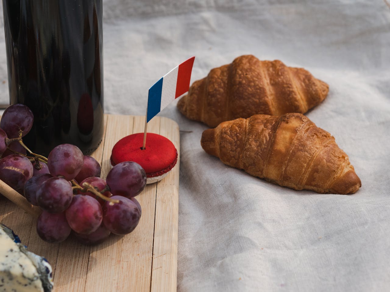 A close-up of French croissants, red macaron, and grapes with a French flag, perfect for cultural festivities.