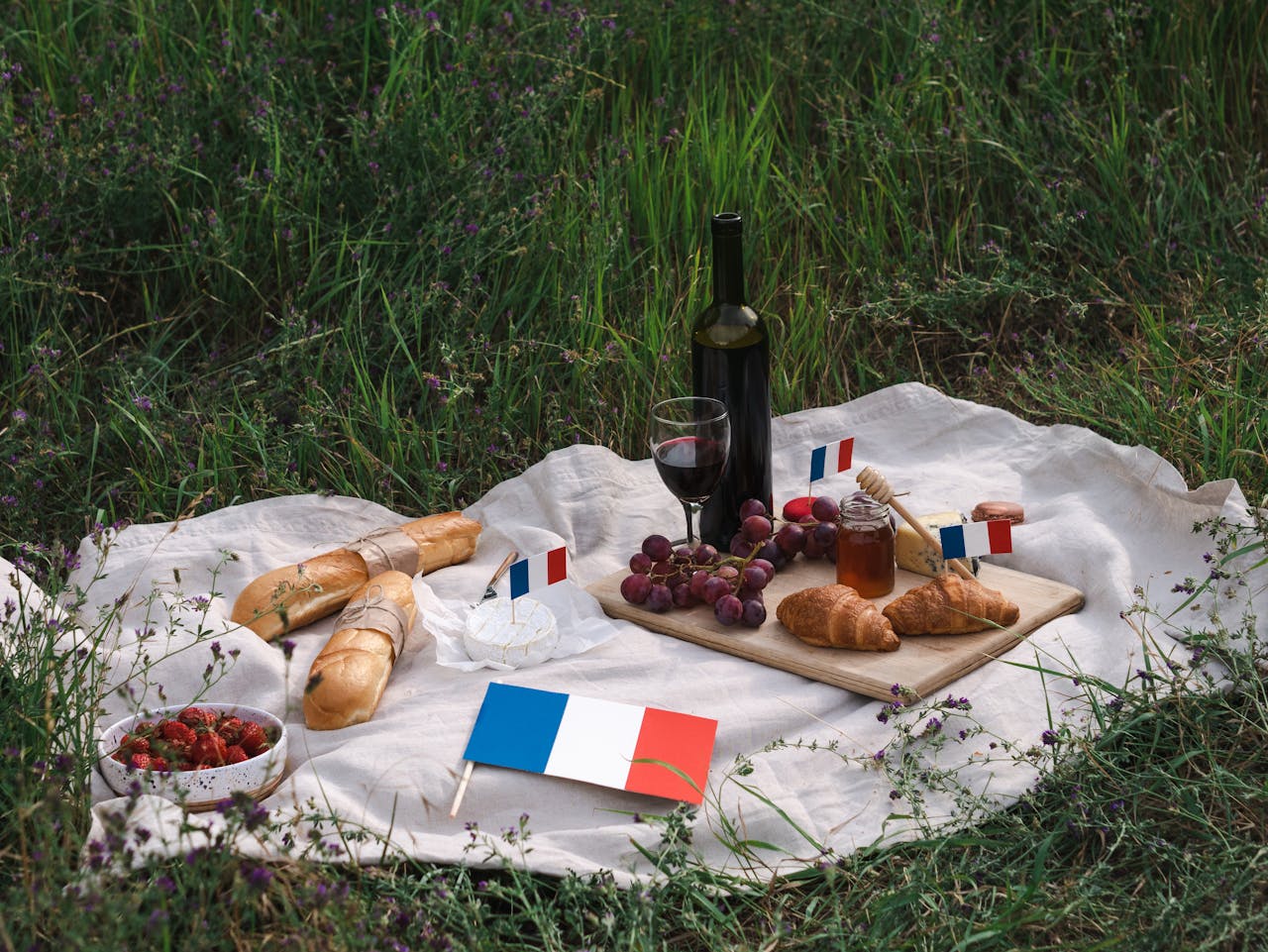 A delightful French picnic scene with baguettes, cheese, wine, and national flags set on a grassy field.